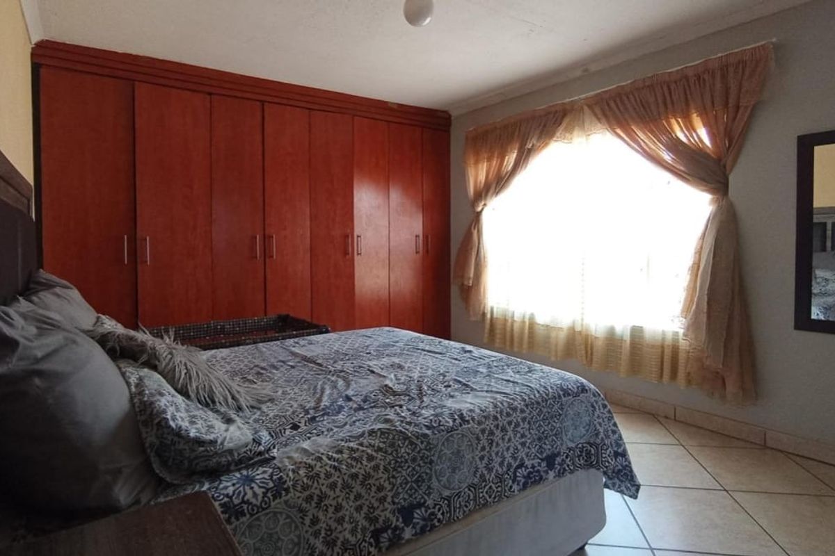 A bedroom featuring built-in wooden cabinetry, tiled flooring, and a large window with curtains.