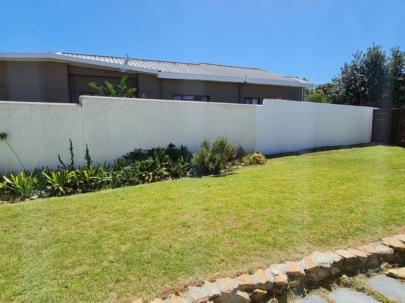 A well-maintained private garden featuring a manicured lawn, stone retaining wall, and secure boundary walling.