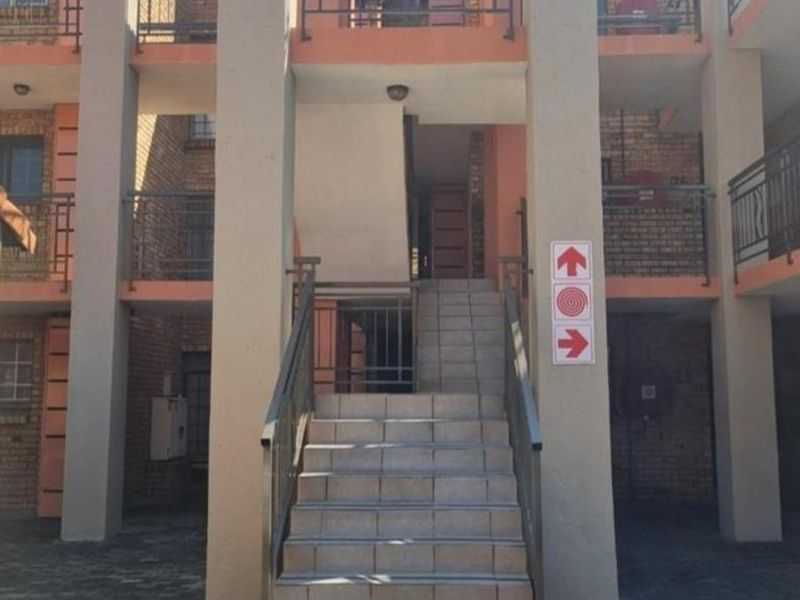 Exterior view of an apartment complex featuring a central tiled staircase, brick facade, and metal railings leading to upper-level residential units.