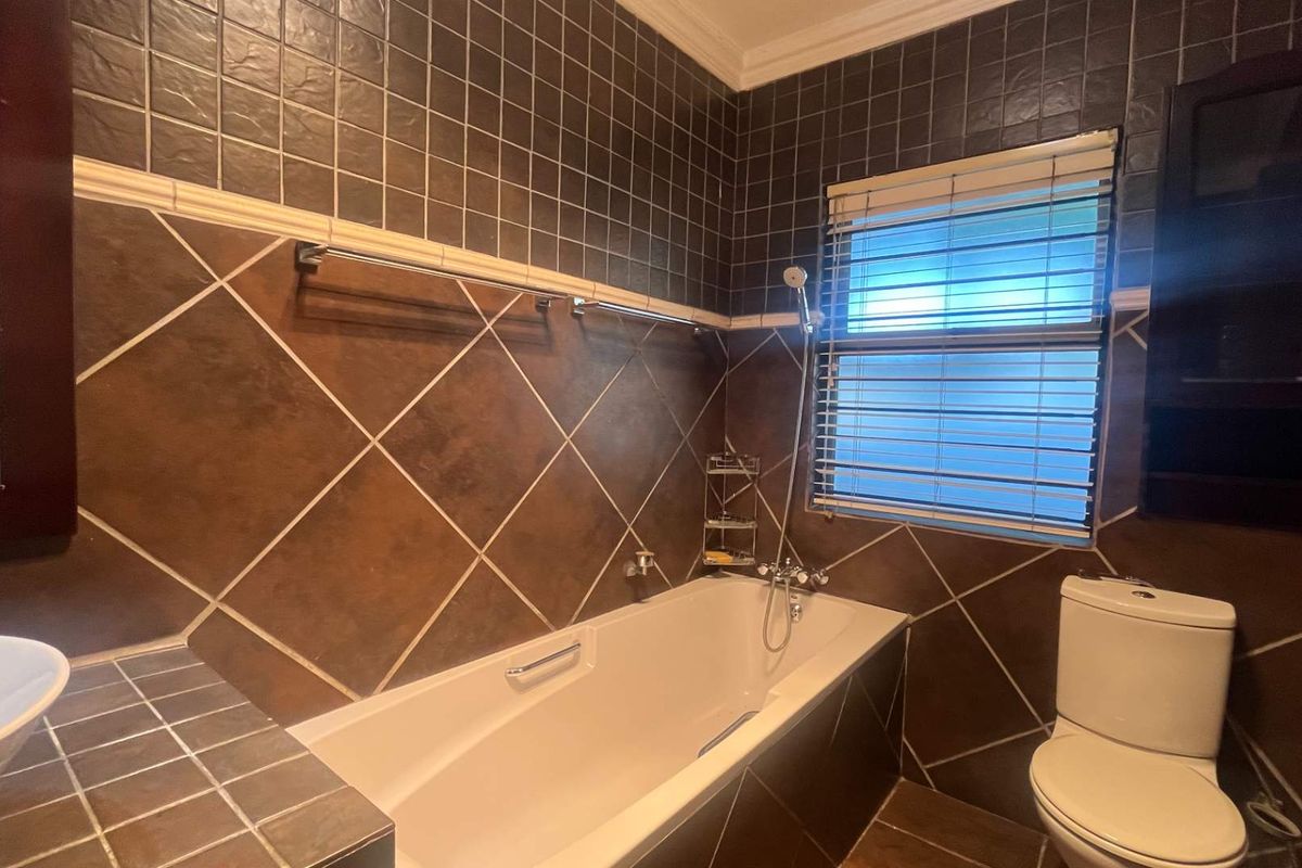 A bathroom featuring a built-in bathtub, toilet, and vessel sink with dark tiled walls and flooring.