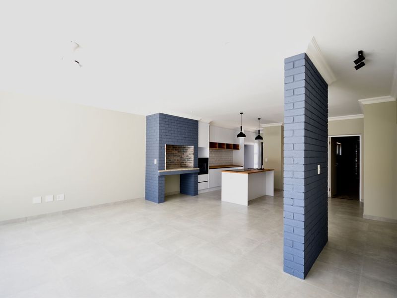 Spacious open-plan living and kitchen area featuring a built-in indoor braai, modern kitchen island, and neutral tiled flooring throughout.