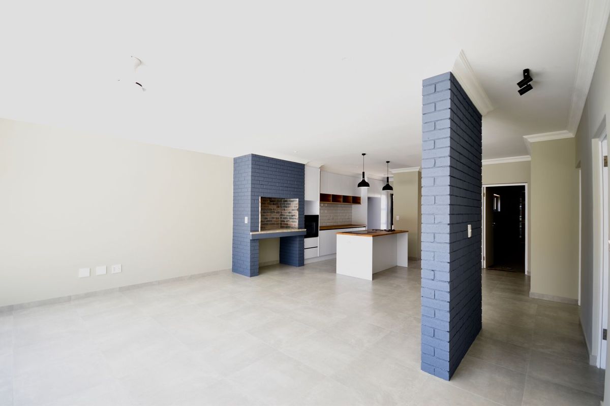 Spacious open-plan living and kitchen area featuring a built-in indoor braai, modern kitchen island, and neutral tiled flooring throughout.