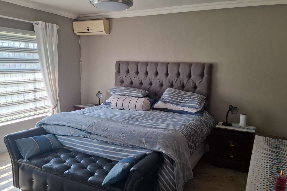 A comfortable bedroom featuring a brick accent wall, crown molding, and a wall-mounted split-system air conditioning unit.