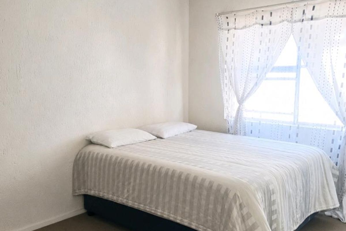 A simple bedroom featuring neutral wall finishes, carpeted flooring, and a window with natural light.