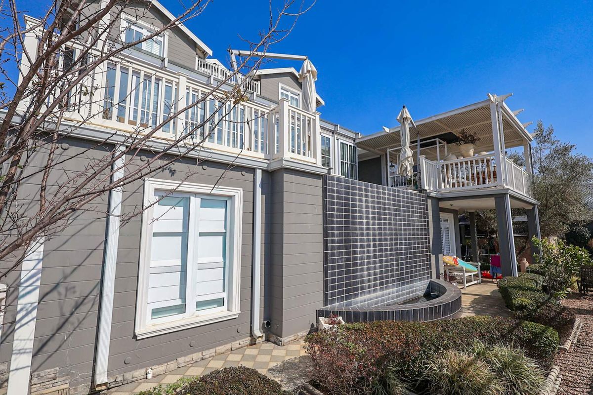 Rear exterior view featuring a modern tiled water feature, raised balcony with pergola, and well-maintained landscaped garden area.