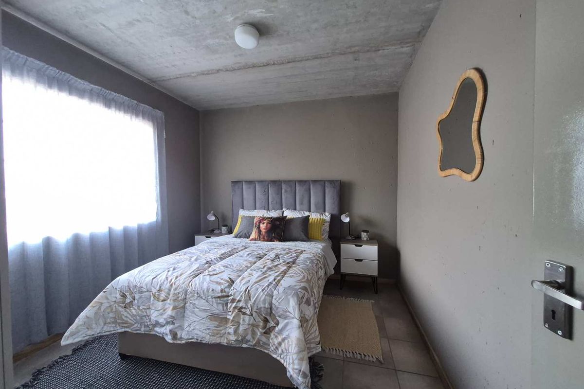 A bedroom featuring an exposed concrete ceiling, tiled flooring, and neutral wall finishes, providing a modern industrial aesthetic.