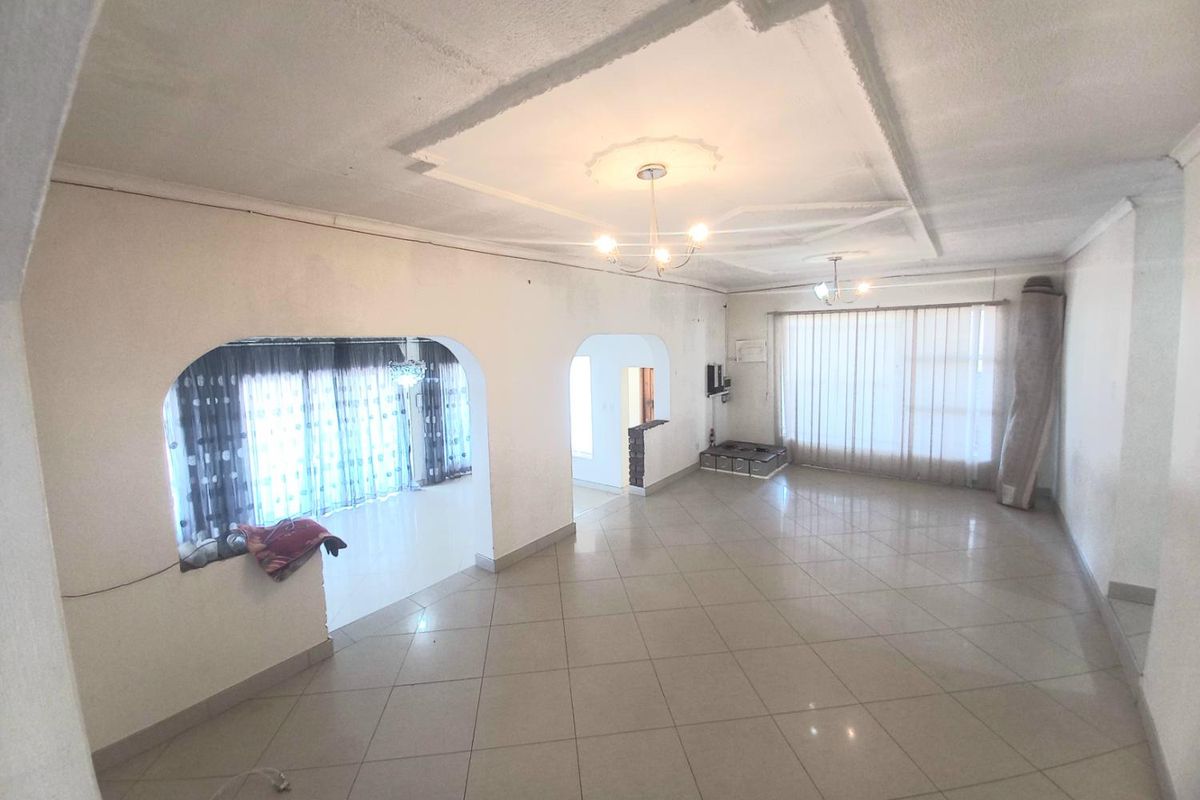 Spacious, open-plan living area featuring neutral tiled flooring, decorative ceiling molding, and arched transitions between rooms, offering a blank canvas for interior design.