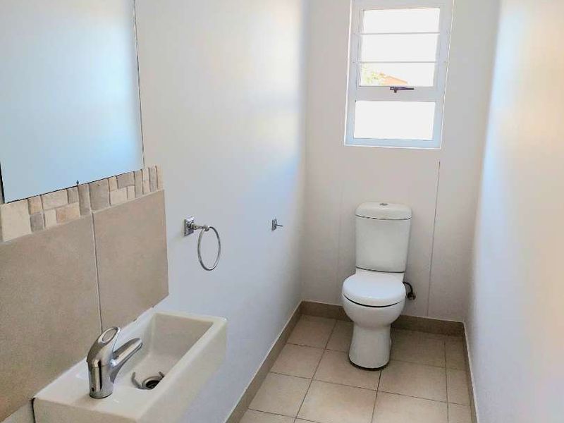 A clean and functional guest bathroom featuring a wall-mounted basin, tiled splashback, and a standard toilet with neutral floor tiling.