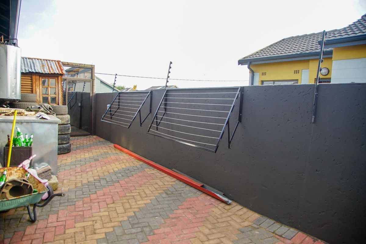 A paved outdoor utility area featuring a perimeter boundary wall with mounted folding clotheslines and security electric fencing.