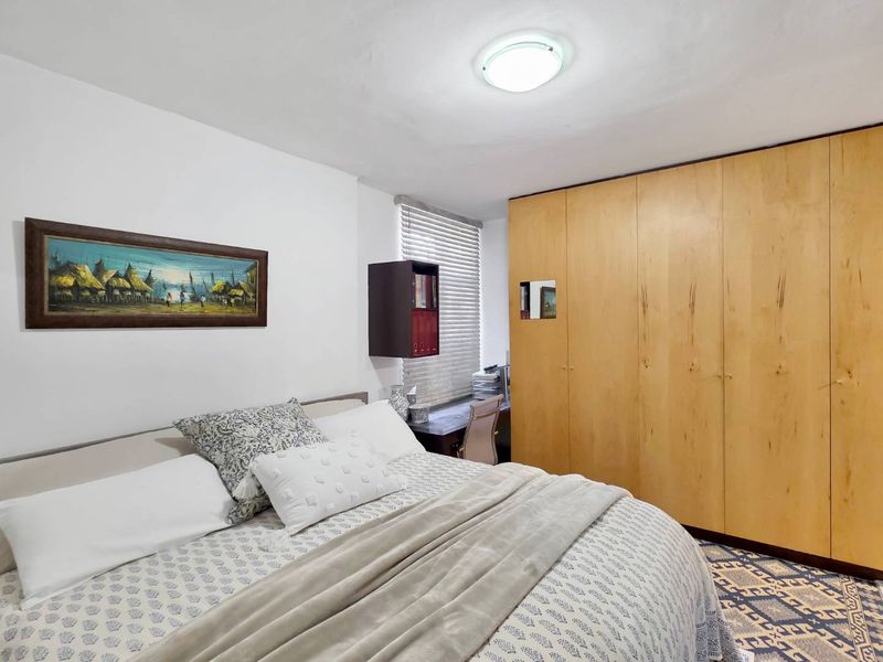 A functional bedroom featuring a large built-in wooden wardrobe, venetian blinds, and a neutral color palette, offering practical storage and comfortable living space.