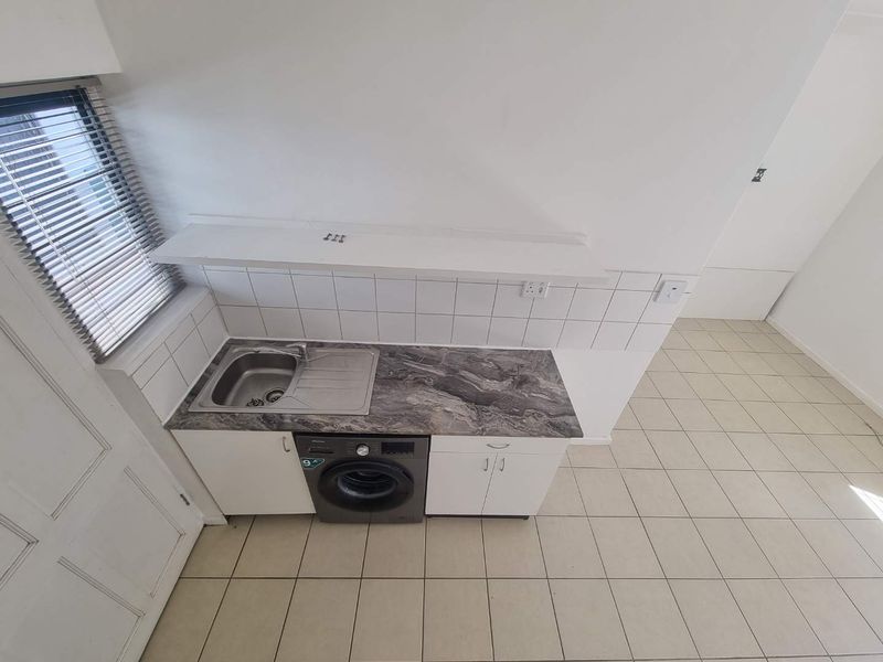 A functional laundry area featuring a stainless steel sink, laminate countertop, tiled backsplash, and built-in cabinetry with ceramic floor tiles.