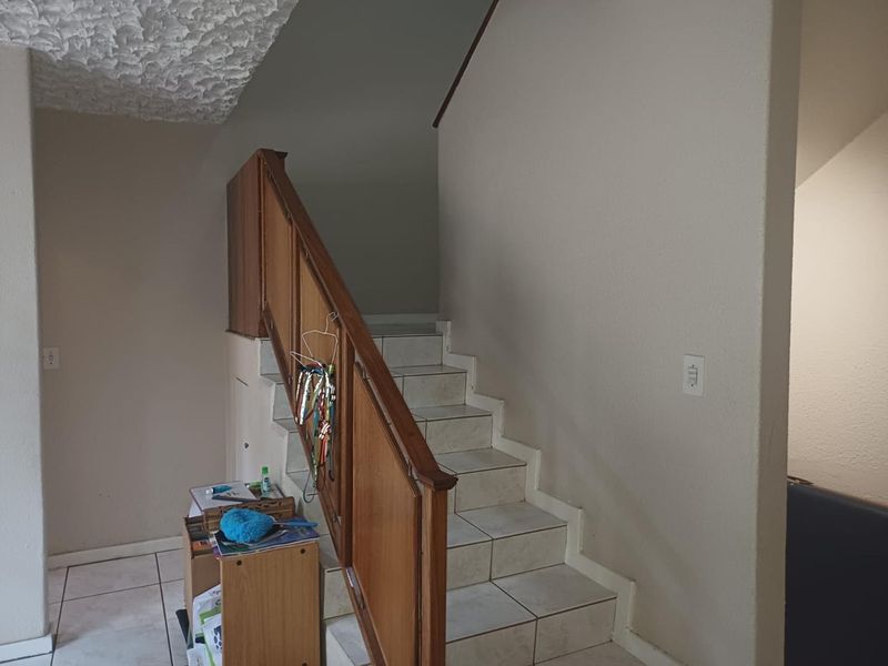 A functional hallway featuring a tiled staircase with a wooden balustrade and a textured ceiling.