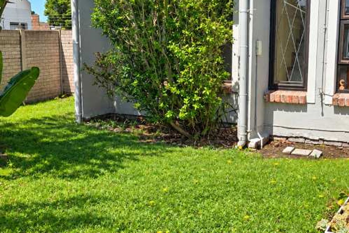 A view of the rear garden area featuring a lawn, brick paving, and the exterior wall of the townhouse.