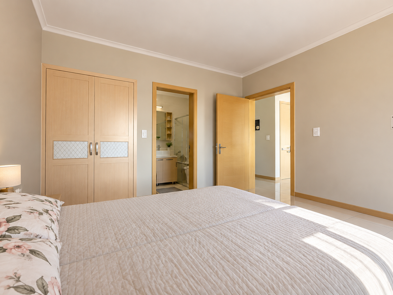 A well-maintained bedroom featuring built-in wooden cupboards, tiled flooring, and direct access to an en-suite bathroom.