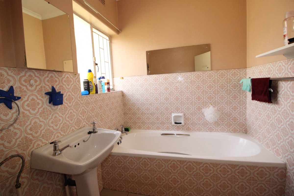 A dated bathroom featuring a pedestal sink, a standard bathtub with wall-mounted taps, and patterned ceramic wall tiles.