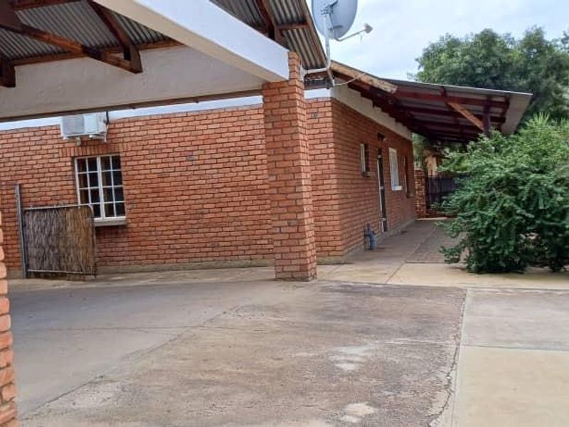 Rear exterior view of the property featuring an exposed brick facade, a covered patio area, and a concrete driveway.