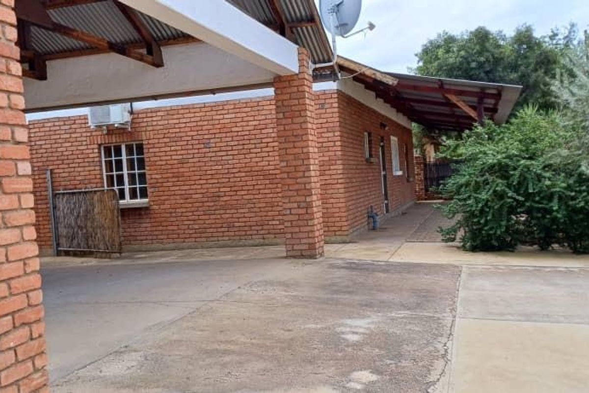 Rear exterior view of the property featuring an exposed brick facade, a covered patio area, and a concrete driveway.