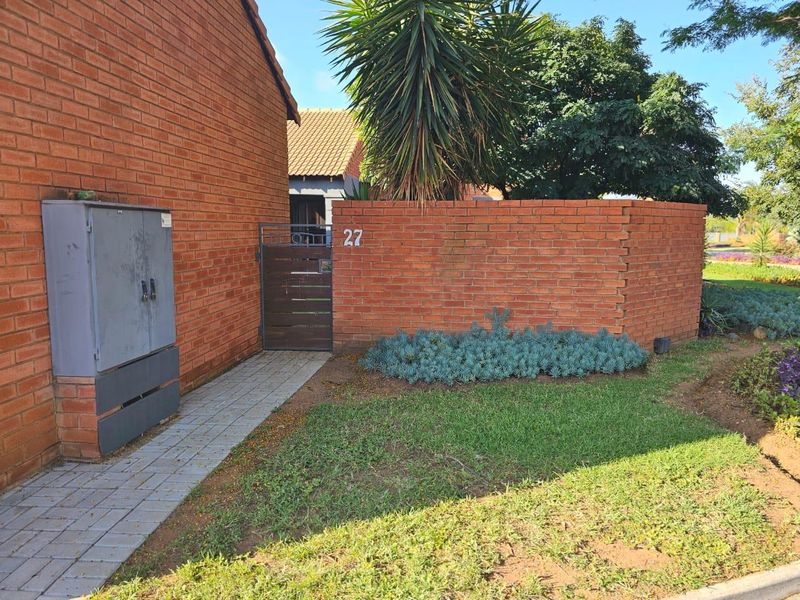 Front entrance view of the townhouse featuring a brick boundary wall, paved walkway, and a private timber pedestrian gate.