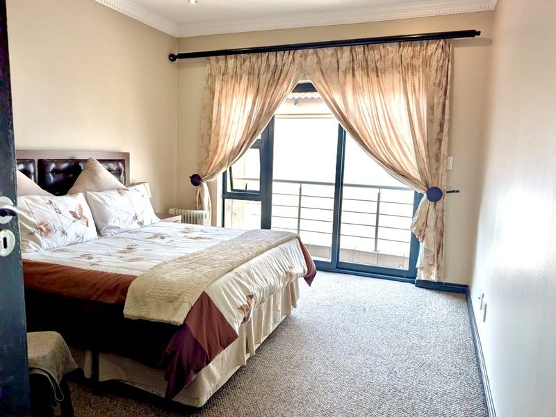 A well-lit bedroom featuring carpeted flooring, coving, and a sliding glass door that opens onto a balcony.