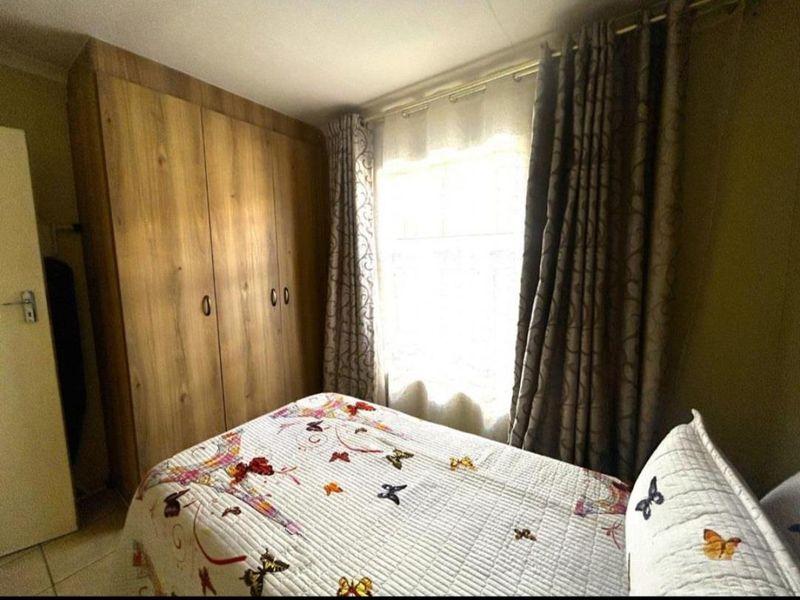 A bedroom featuring built-in wooden wardrobes, tiled flooring, and a window with curtains.