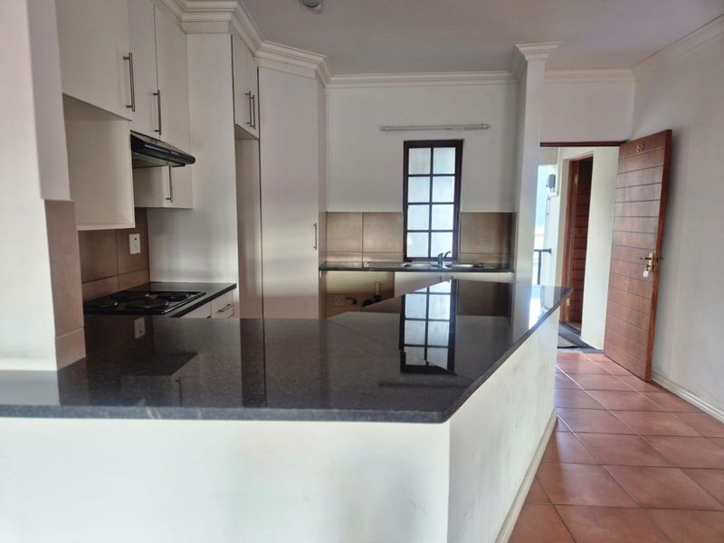A clean, functional kitchen featuring granite countertops, ample built-in cabinetry, an electric hob with extractor fan, and tiled flooring.