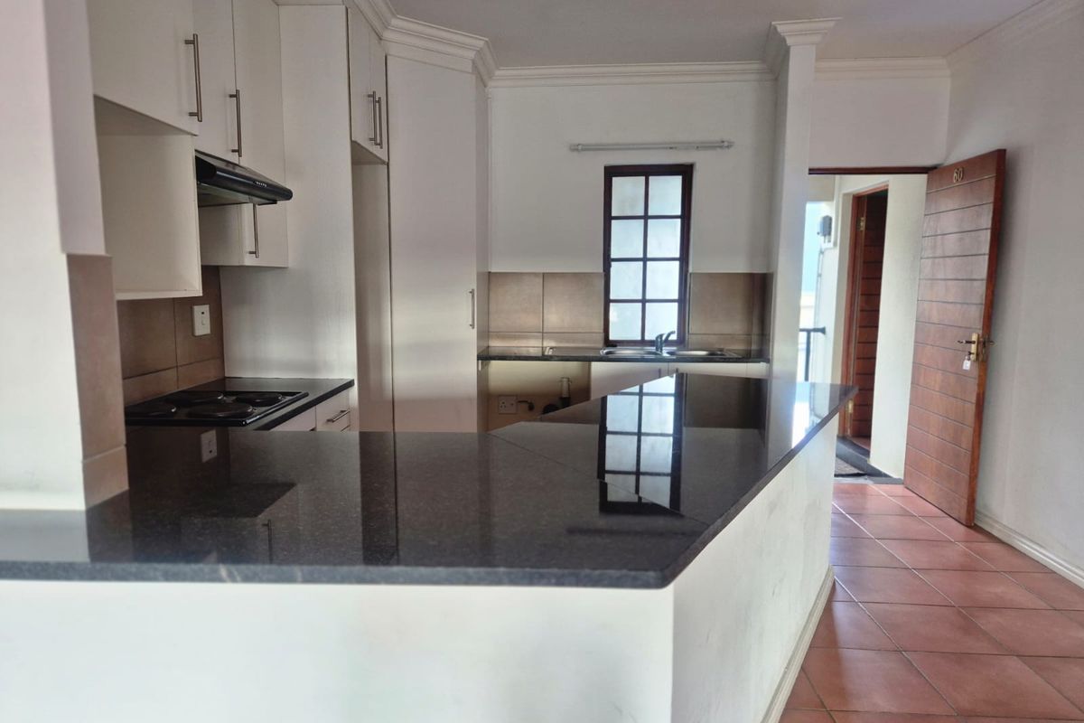 A clean, functional kitchen featuring granite countertops, ample built-in cabinetry, an electric hob with extractor fan, and tiled flooring.