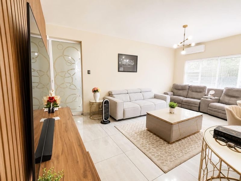 A well-maintained living room featuring a stylish slatted wood accent wall, polished tile flooring, and a modern chandelier, creating a bright and inviting atmosphere.