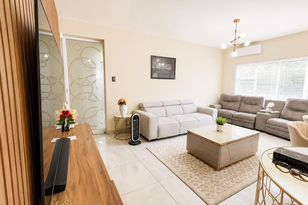 A well-maintained living room featuring a stylish slatted wood accent wall, polished tile flooring, and a modern chandelier, creating a bright and inviting atmosphere.