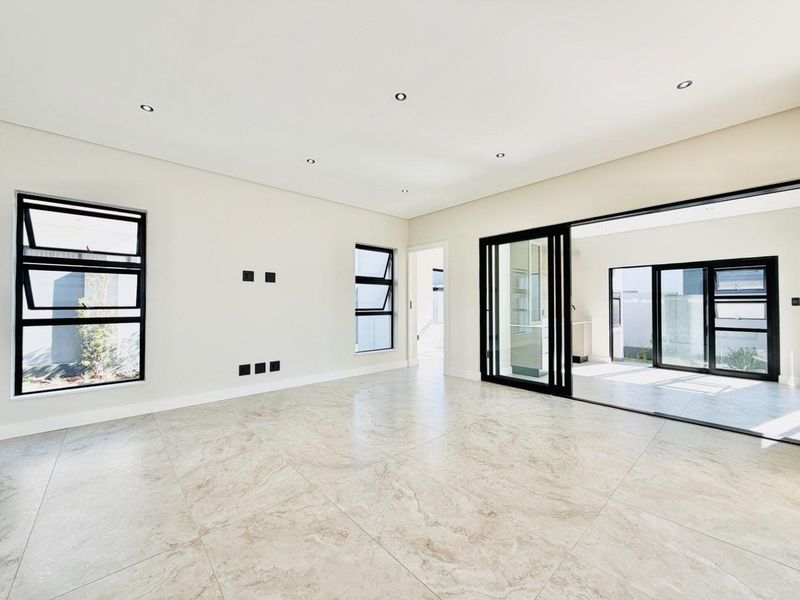 A bright, modern, and spacious living area featuring large-format tiled flooring, recessed lighting, and expansive sliding glass doors leading to an outdoor space.