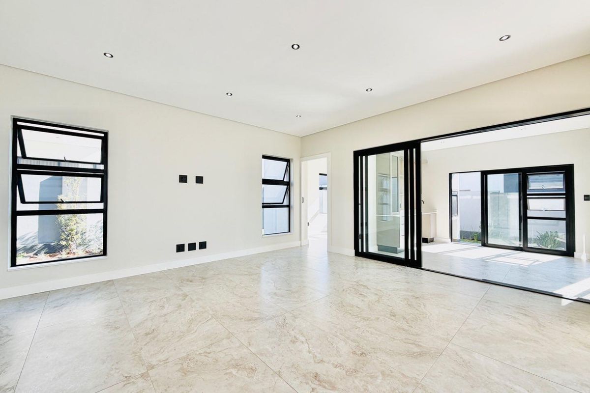 A bright, modern, and spacious living area featuring large-format tiled flooring, recessed lighting, and expansive sliding glass doors leading to an outdoor space.