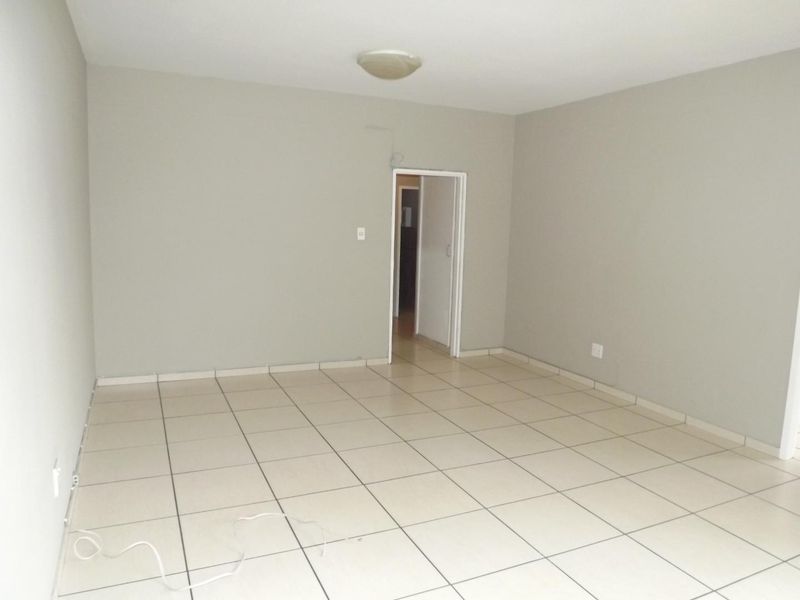 A vacant, neutrally painted living area featuring light-colored floor tiles and a simple flush mount ceiling light fixture.