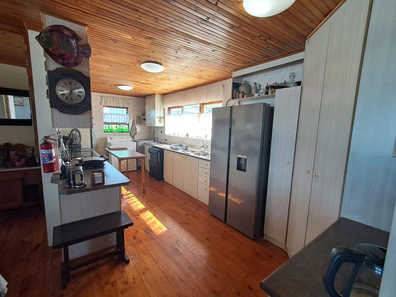 A functional kitchen featuring timber ceiling and flooring, ample built-in cabinetry, and a double sink, offering a traditional aesthetic with potential for modernization.