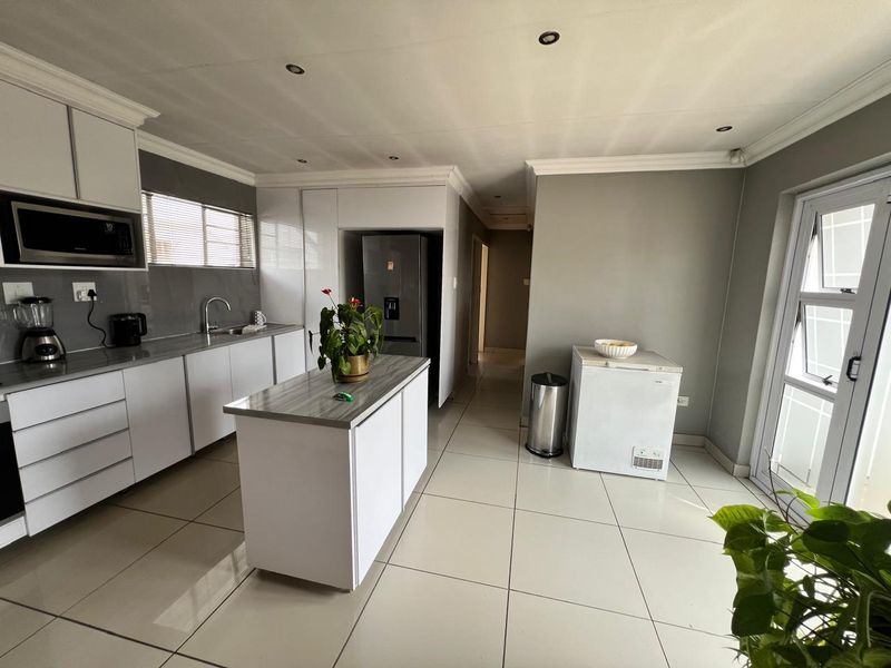 Modern kitchen featuring white cabinetry, a central island with laminate countertop, tiled flooring, and recessed lighting, offering a clean and functional workspace.