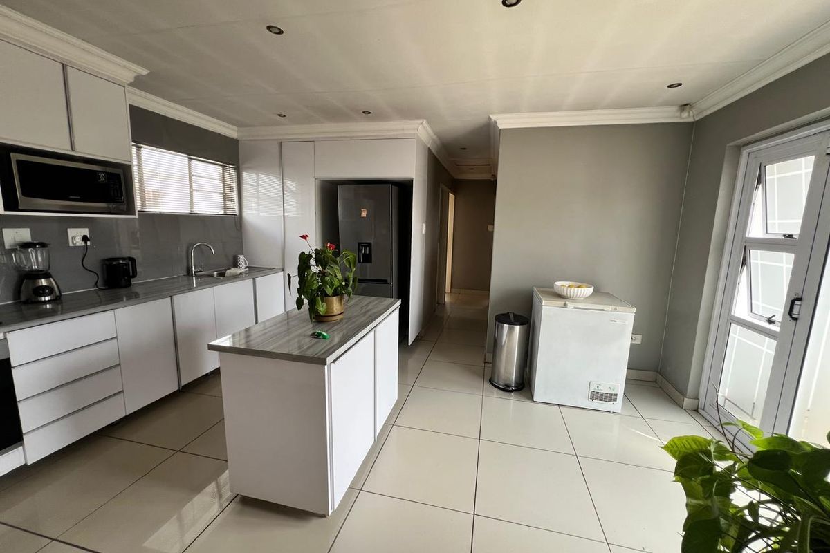 Modern kitchen featuring white cabinetry, a central island with laminate countertop, tiled flooring, and recessed lighting, offering a clean and functional workspace.