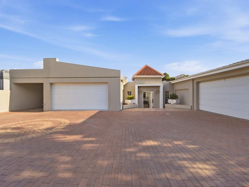 Front elevation of a modern house featuring a spacious paved driveway, multiple garage doors, and a covered entrance with a tiled roof.