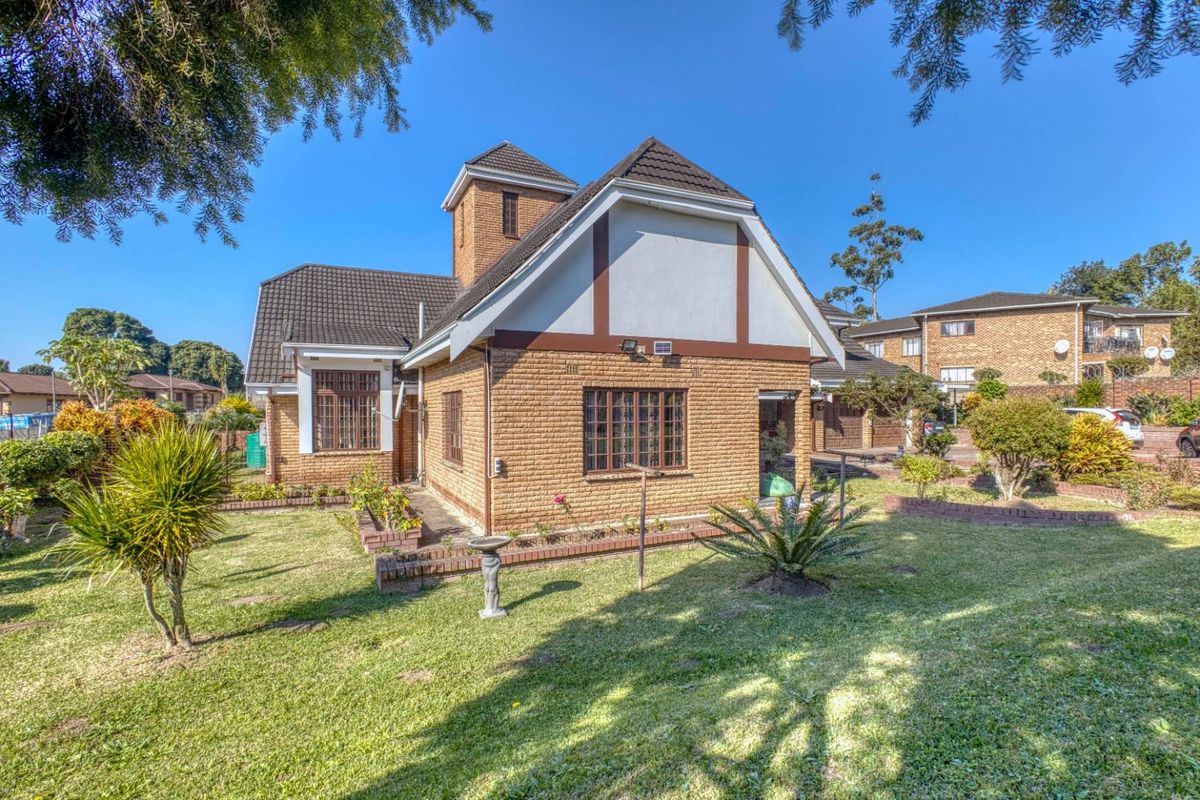 A well-maintained brick house exterior featuring a tiled roof, security bars on windows, and a landscaped garden with established lawn and brick edging.