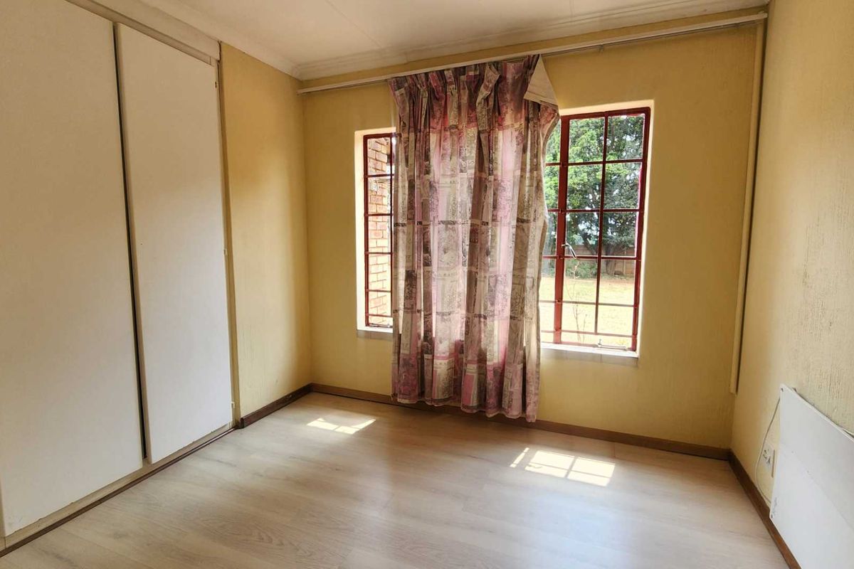 A bedroom featuring light wood-look flooring, built-in sliding door cupboards, and large windows with security bars.