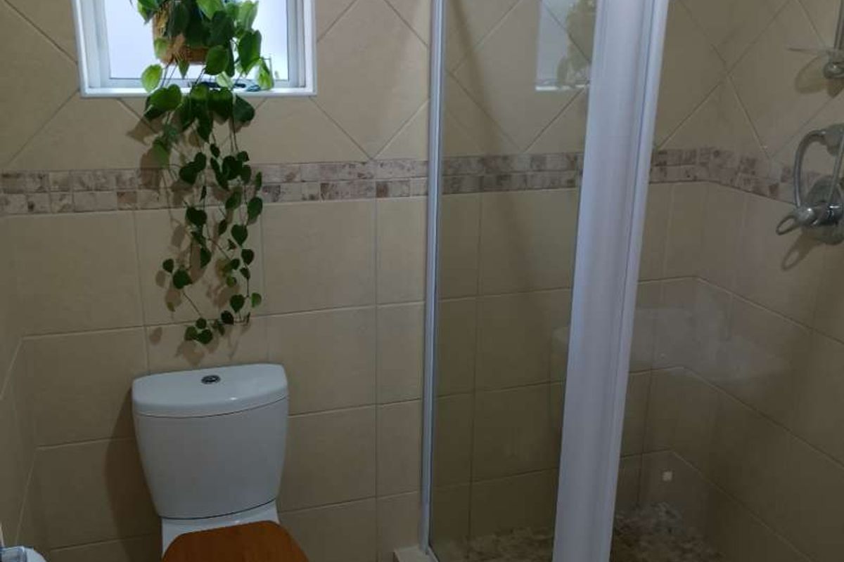 A functional bathroom featuring a corner shower enclosure with glass doors, a standard toilet, and neutral wall and floor tiling.