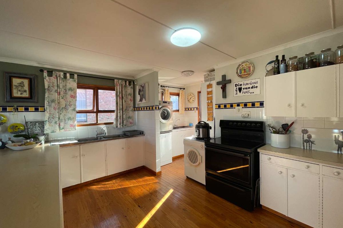 A functional kitchen featuring white cabinetry, timber flooring, a tiled splashback, and a dedicated laundry area with built-in plumbing connections.