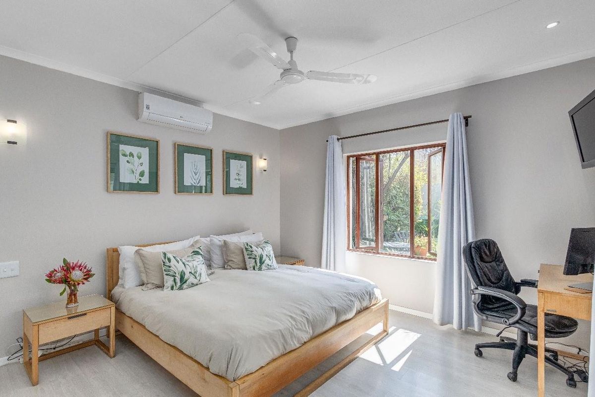 A well-maintained bedroom featuring a ceiling fan, split-system air conditioning, and timber-framed casement windows allowing natural light.