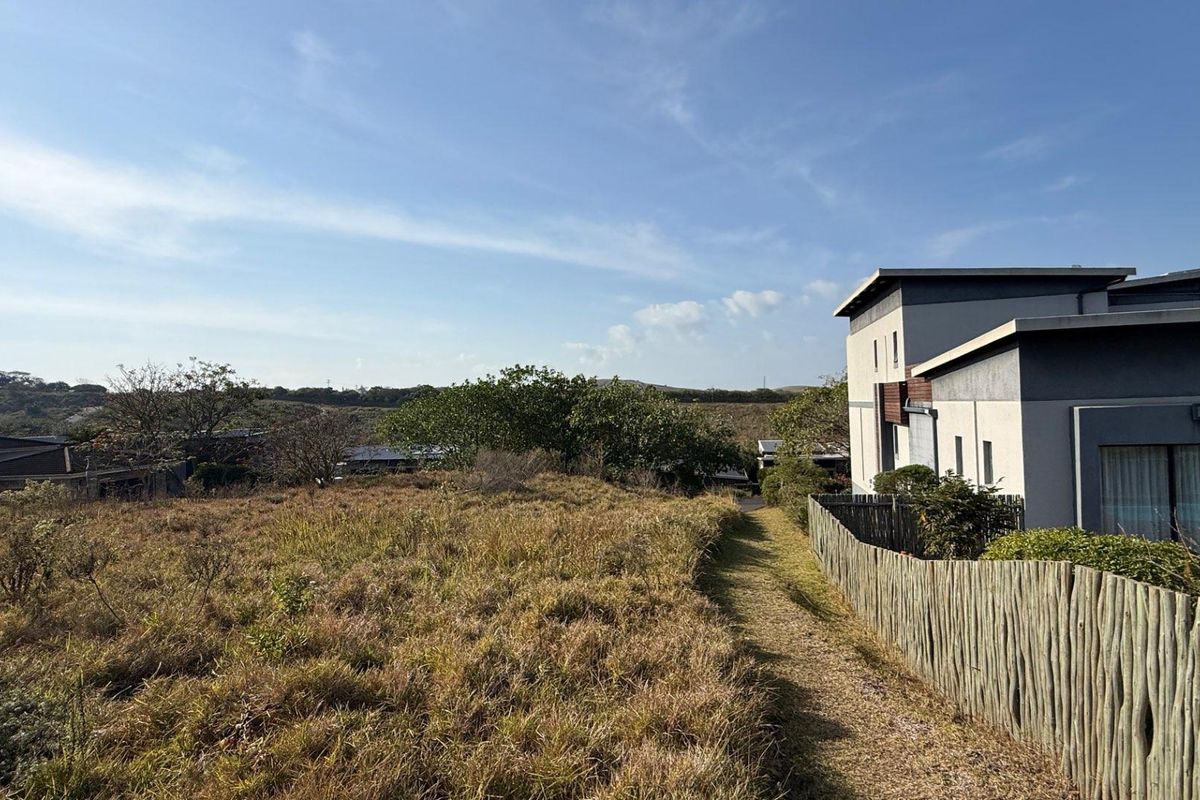 A view of the rear section of the residential property featuring natural grass terrain and wooden pole boundary fencing.