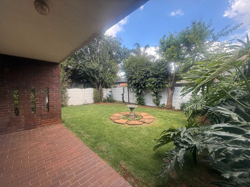 A covered brick-paved patio overlooking a private garden with a well-maintained lawn and secure boundary walling.