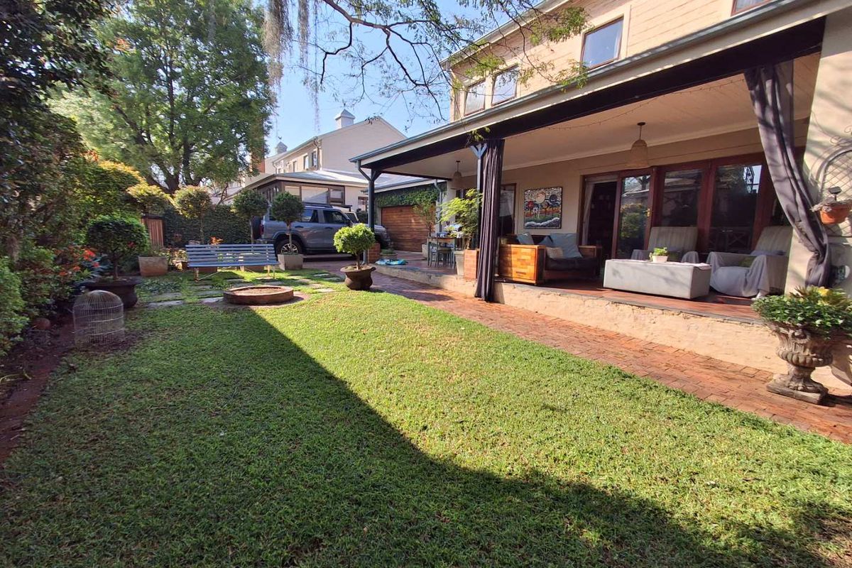 A well-maintained rear garden featuring a covered patio area with brick paving, a lawn, and a built-in fire pit.