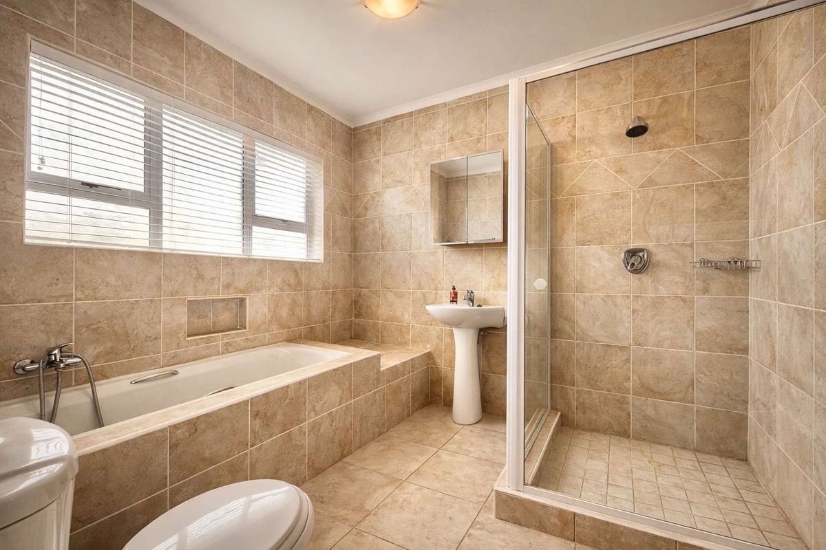 A functional bathroom featuring a tiled bathtub, a separate glass-enclosed shower, a pedestal basin, and a mirrored medicine cabinet.