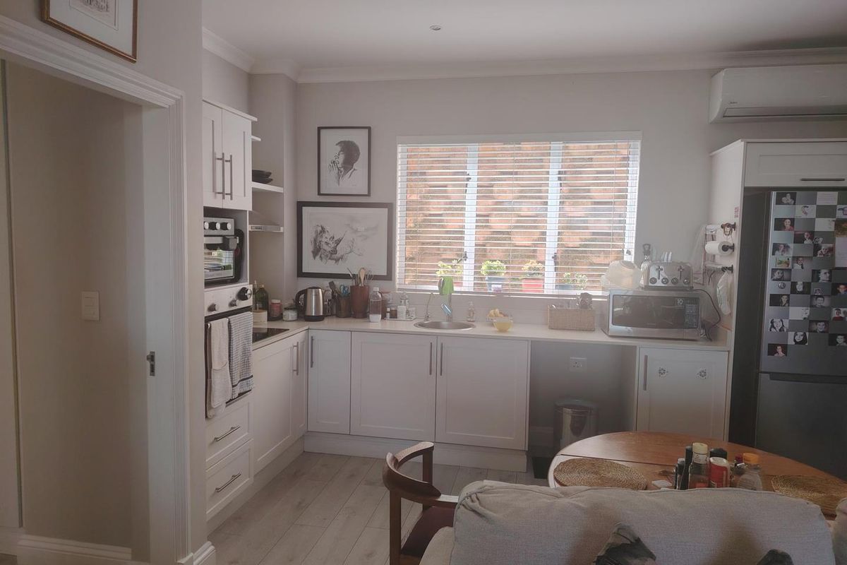 A functional kitchen featuring white cabinetry, built-in oven, hob, stainless steel sink, and laminate flooring, with an integrated air conditioning unit.
