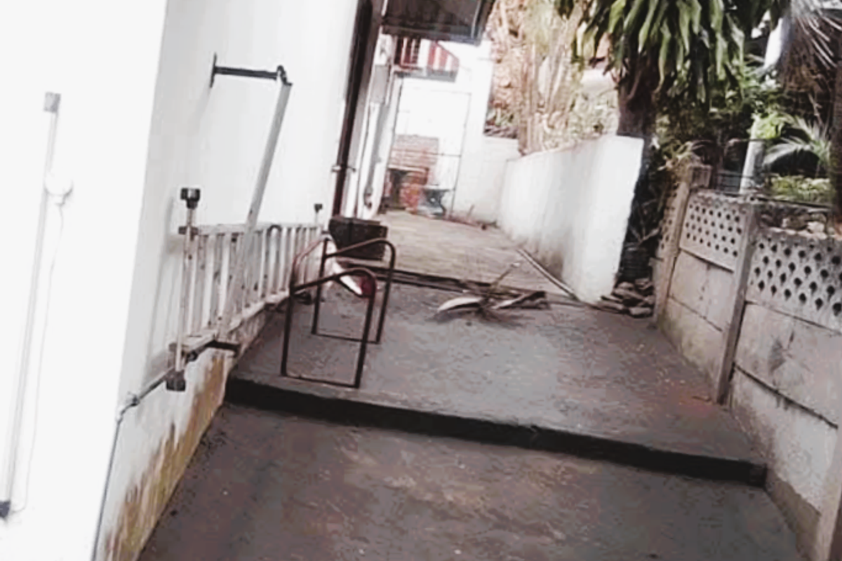 A narrow side exterior area featuring concrete paving, a striped awning, and a boundary wall, showing signs of wear and weathering.