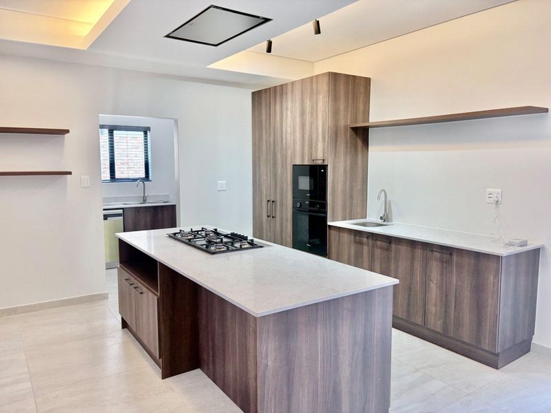 Modern kitchen featuring a central island with gas hob, built-in appliances, stone countertops, and sleek wood-finish cabinetry with integrated lighting.