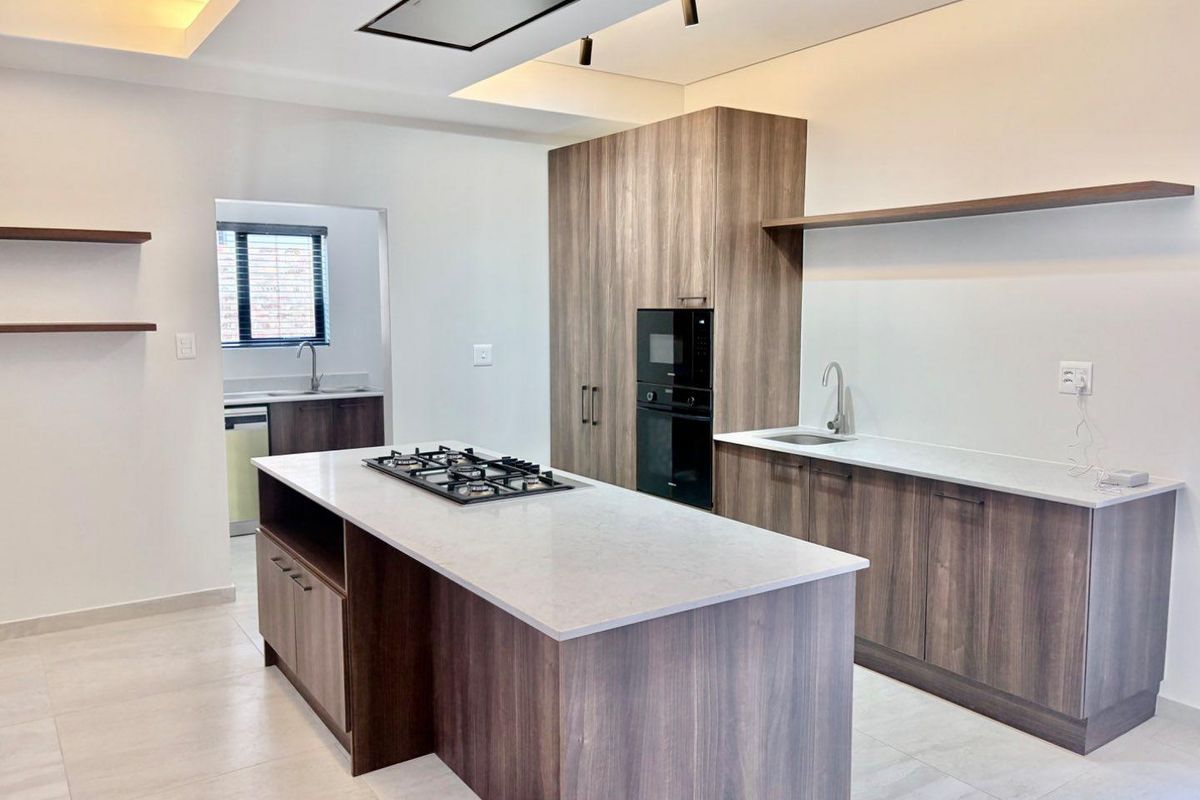 Modern kitchen featuring a central island with gas hob, built-in appliances, stone countertops, and sleek wood-finish cabinetry with integrated lighting.