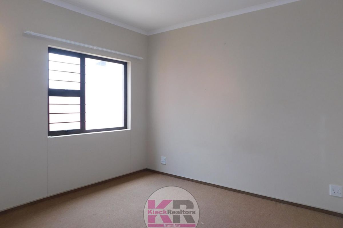 A clean, empty bedroom featuring neutral wall paint, carpeted flooring, and a window fitted with security bars.