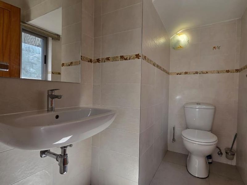 A clean, functional bathroom featuring a wall-mounted basin, chrome fixtures, and neutral wall and floor tiling with a decorative accent border.